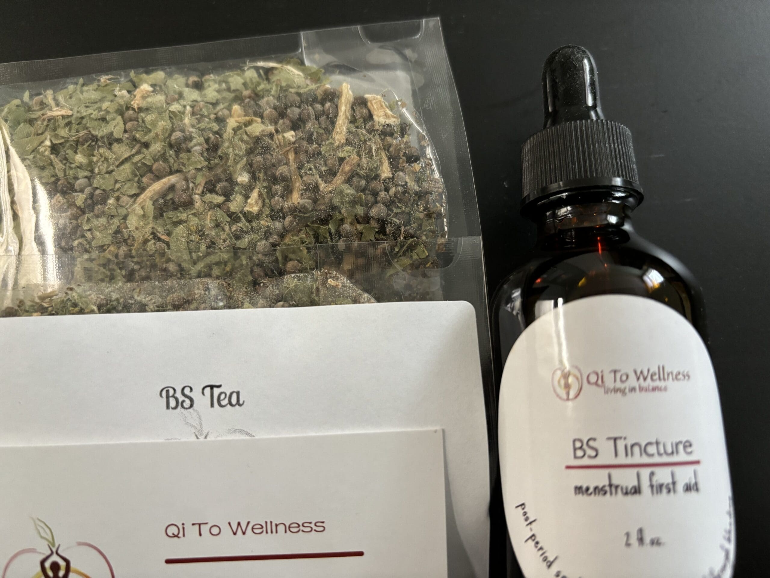 tincture dropper bottle, packet of herbs and business card on black background