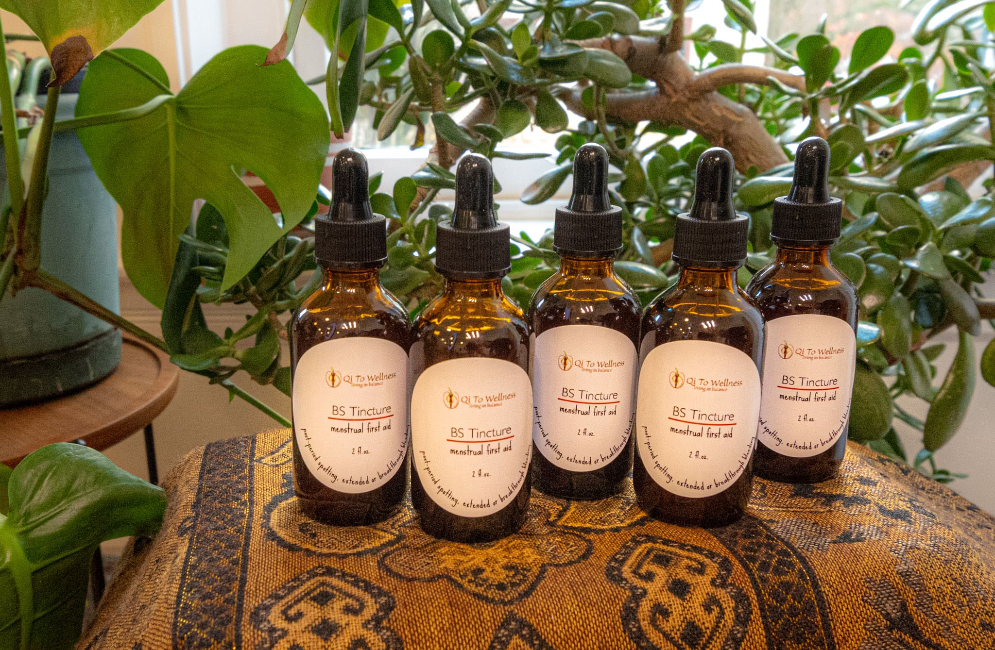 Four dropper bottles of menstrual first aid tincture on a cloth with plants in the backdrop